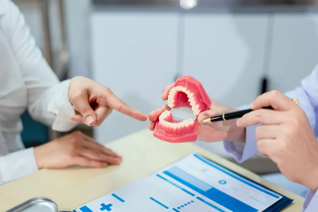 A dentist explains dental health to a patient while holding a dental model, demonstrating oral care and treatment procedures in a clinical consultation setting