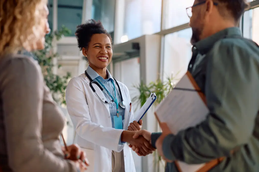Happy doctor handshaking with her patients at medical clinic.