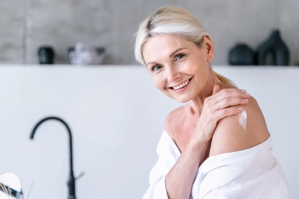 Woman applying body cream on shoulder and enjoying cosmetic effect